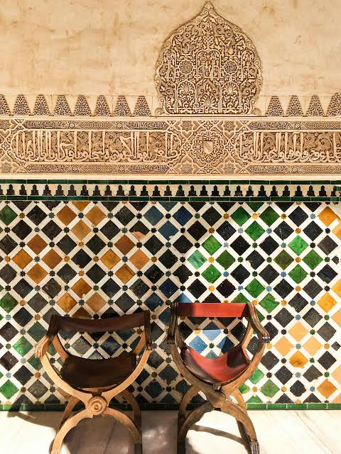 Multicoloured zellige tilework and carved stucco inscription in the Alhambra palace of Granada — the same decorative tradition that was carried to Morocco and is still practised by craftsmen in Fes today